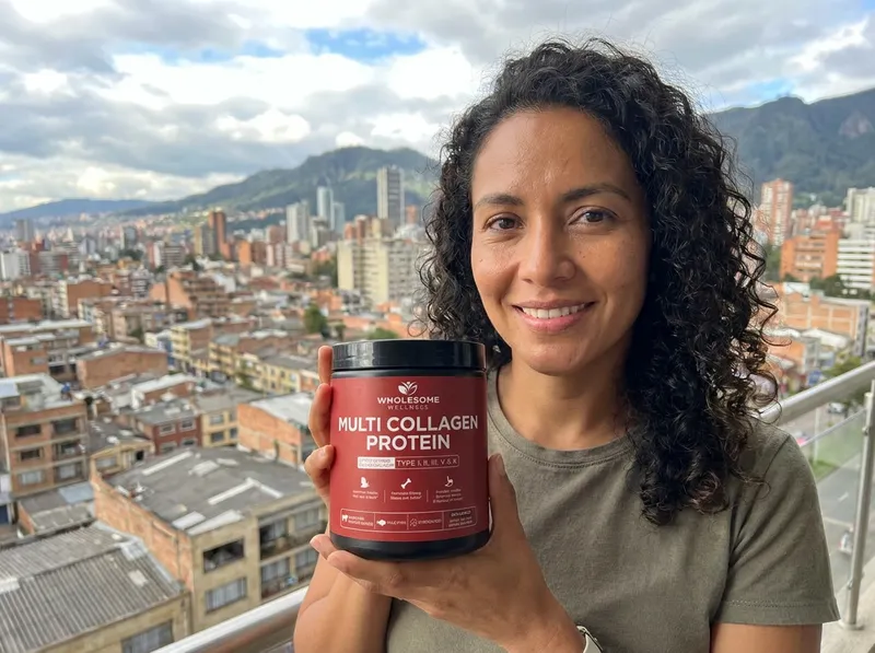 Mujer de 35 años en un balcón en Bogotá, sosteniendo el tarro de colágeno con una sonrisa.