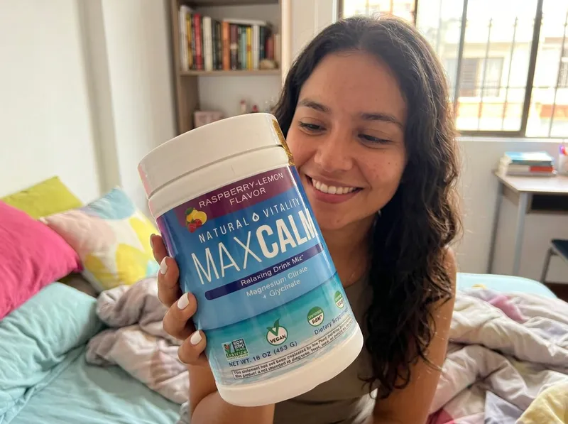 Joven colombiana de 24 años sentada en su habitación en Cali, sosteniendo el tarro de magnesio MaxCalm con una sonrisa.