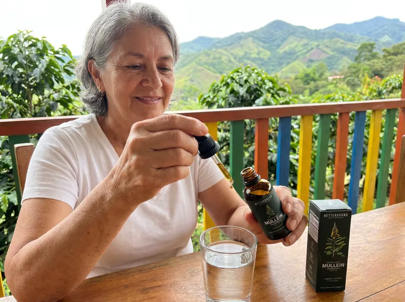 Señora colombiana en el corredor de una finca cafetera poniendo las gotas en un vaso de agua