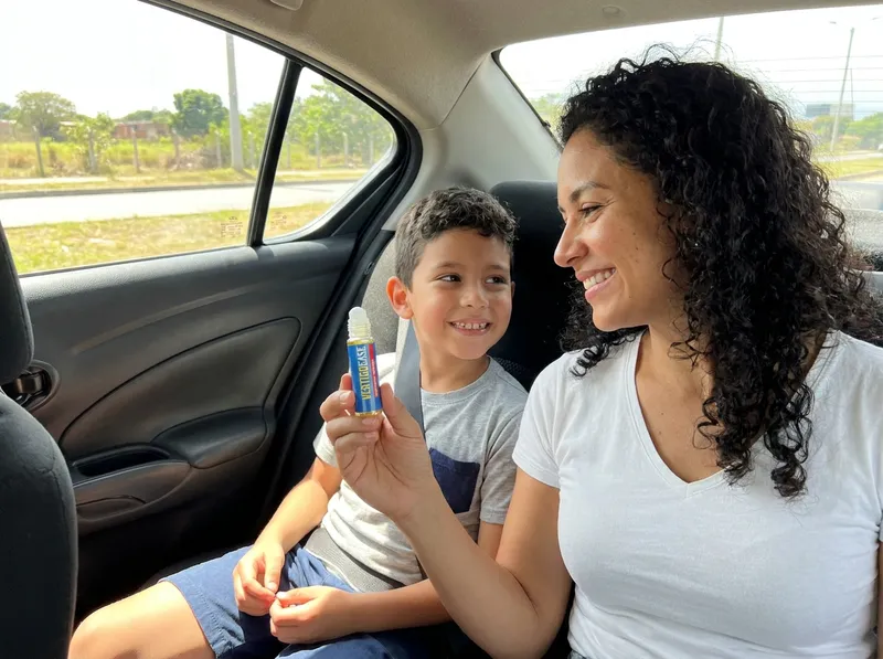 Mamá con su hijo en el asiento de atrás del carro, con el roll-on Vertigo Ease en la mano